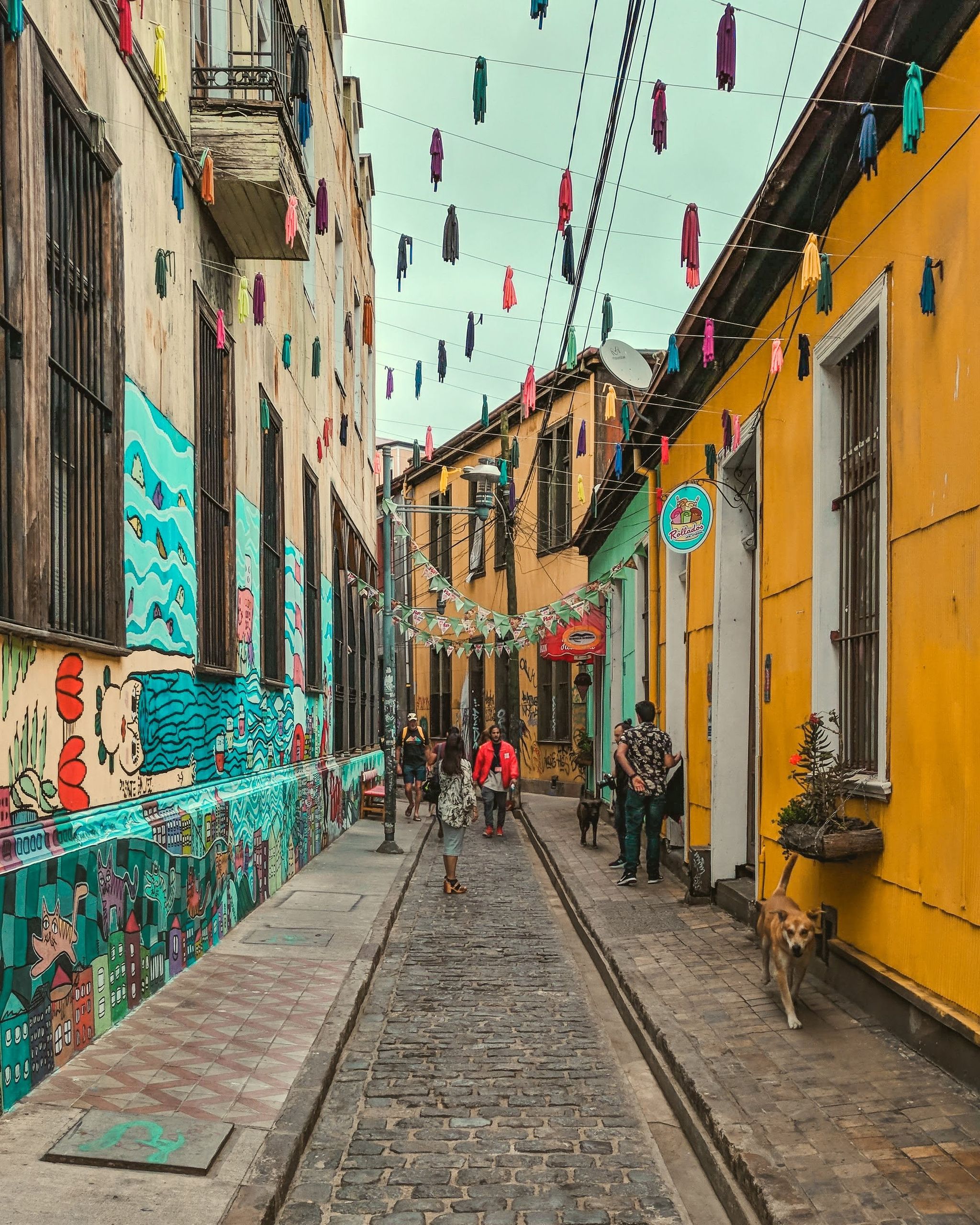Colorful alley decorated with graffiti and vibrant hanging flags, capturing urban street life.